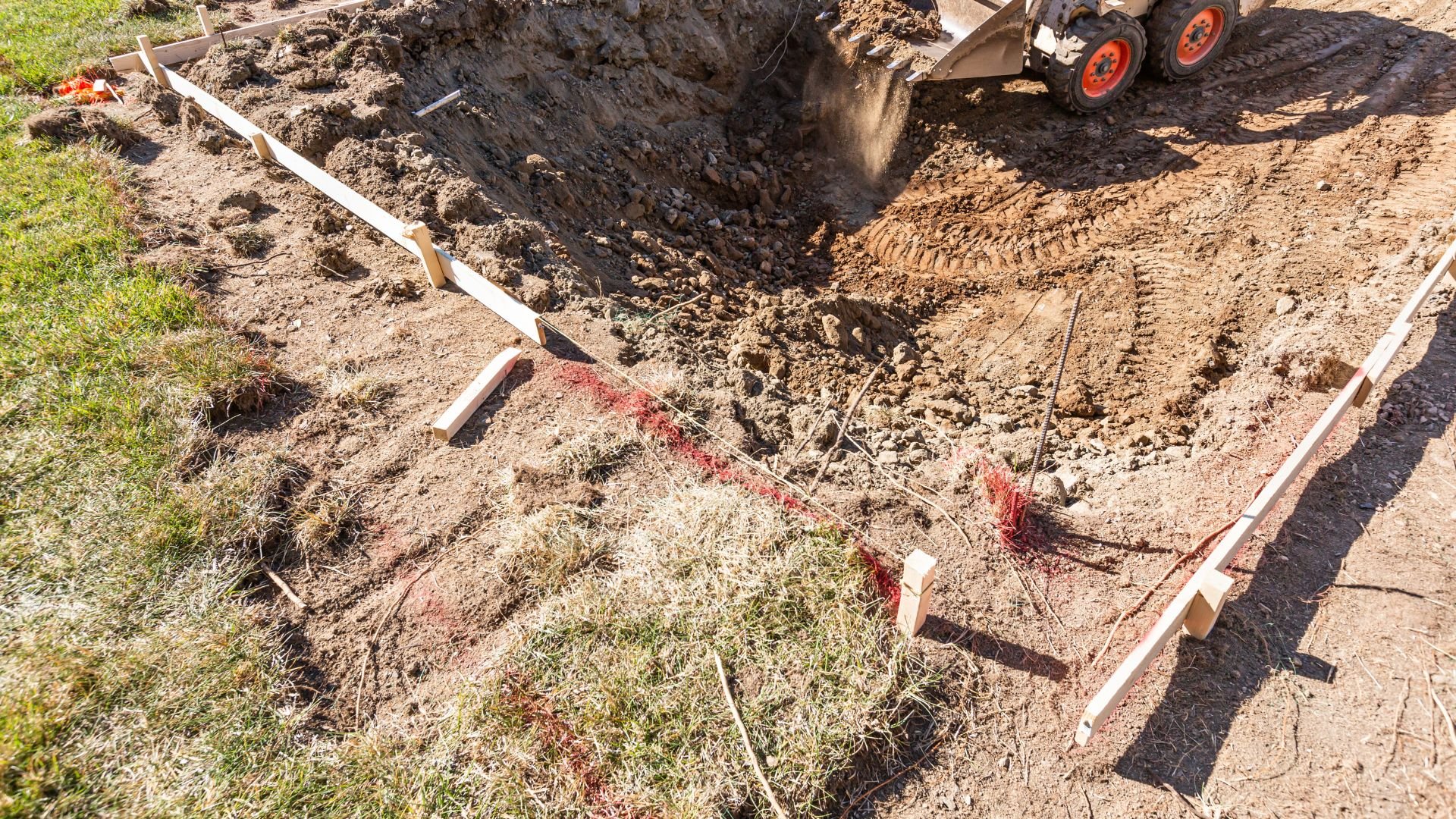 Construction site with excavated ground, wooden stakes, and digging equipment