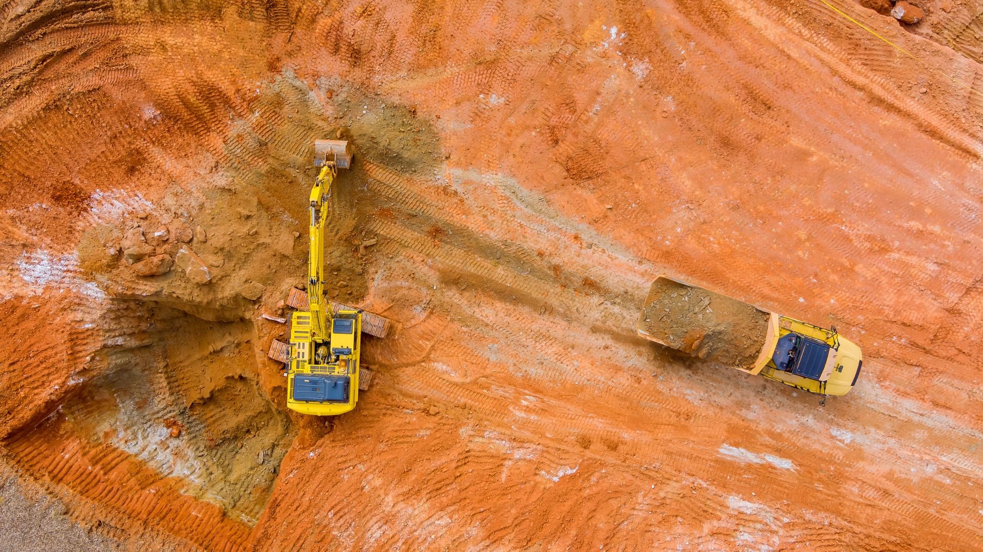 Yellow excavators working in a red clay quarry from aerial view