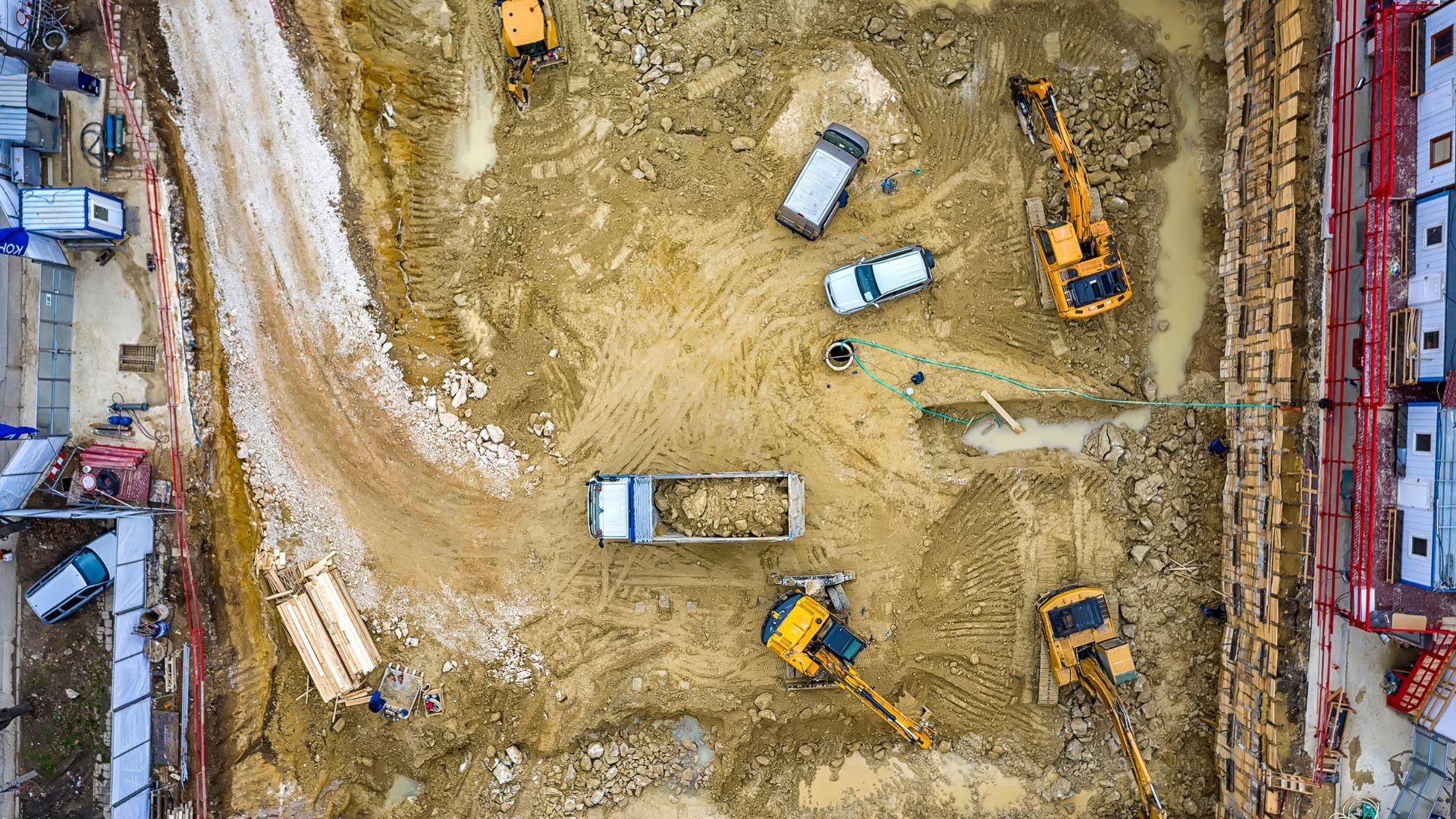 Aerial view of construction site with excavators, trucks, and muddy terrain