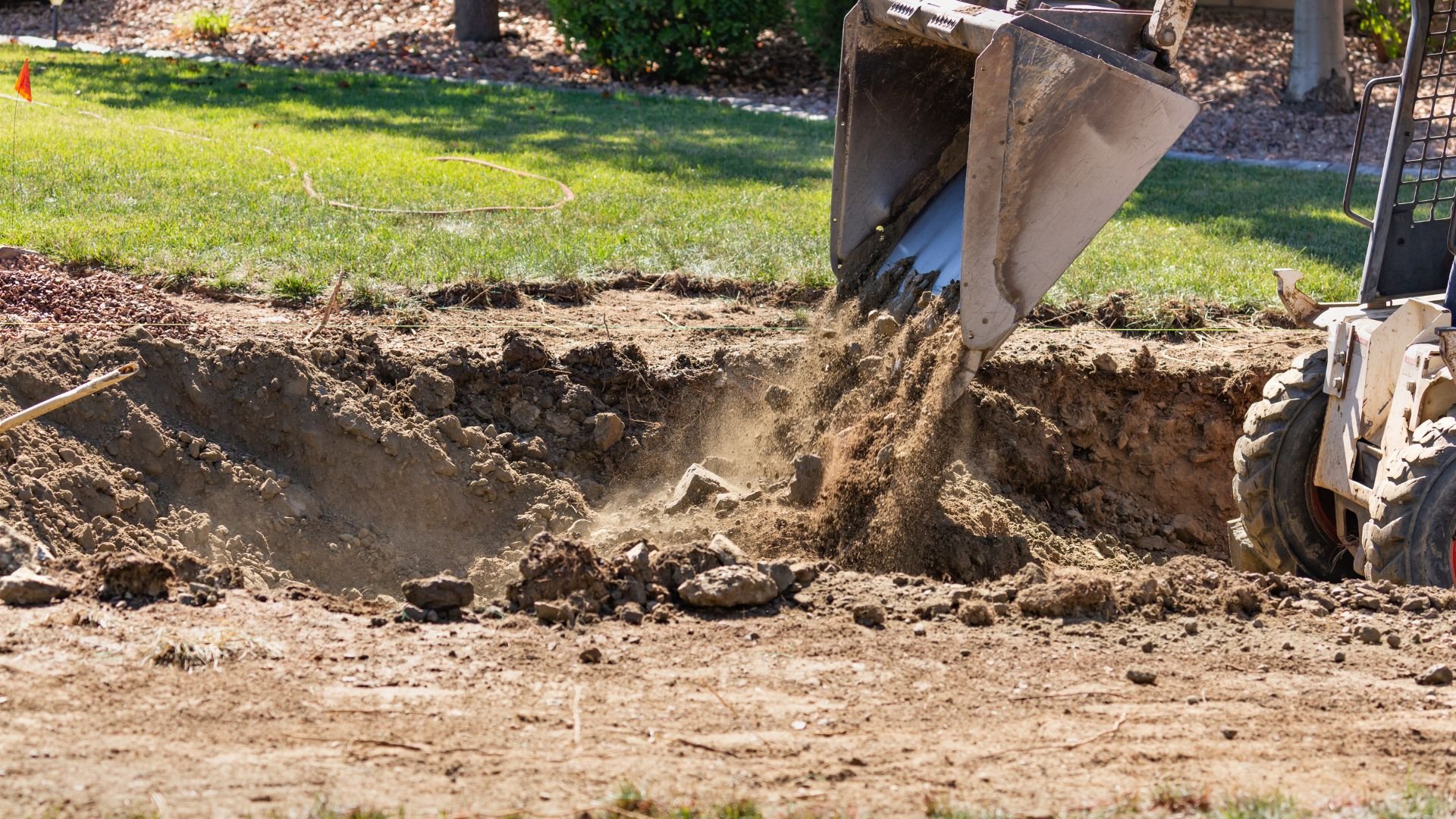 Excavator digging a large hole in a grassy backyard