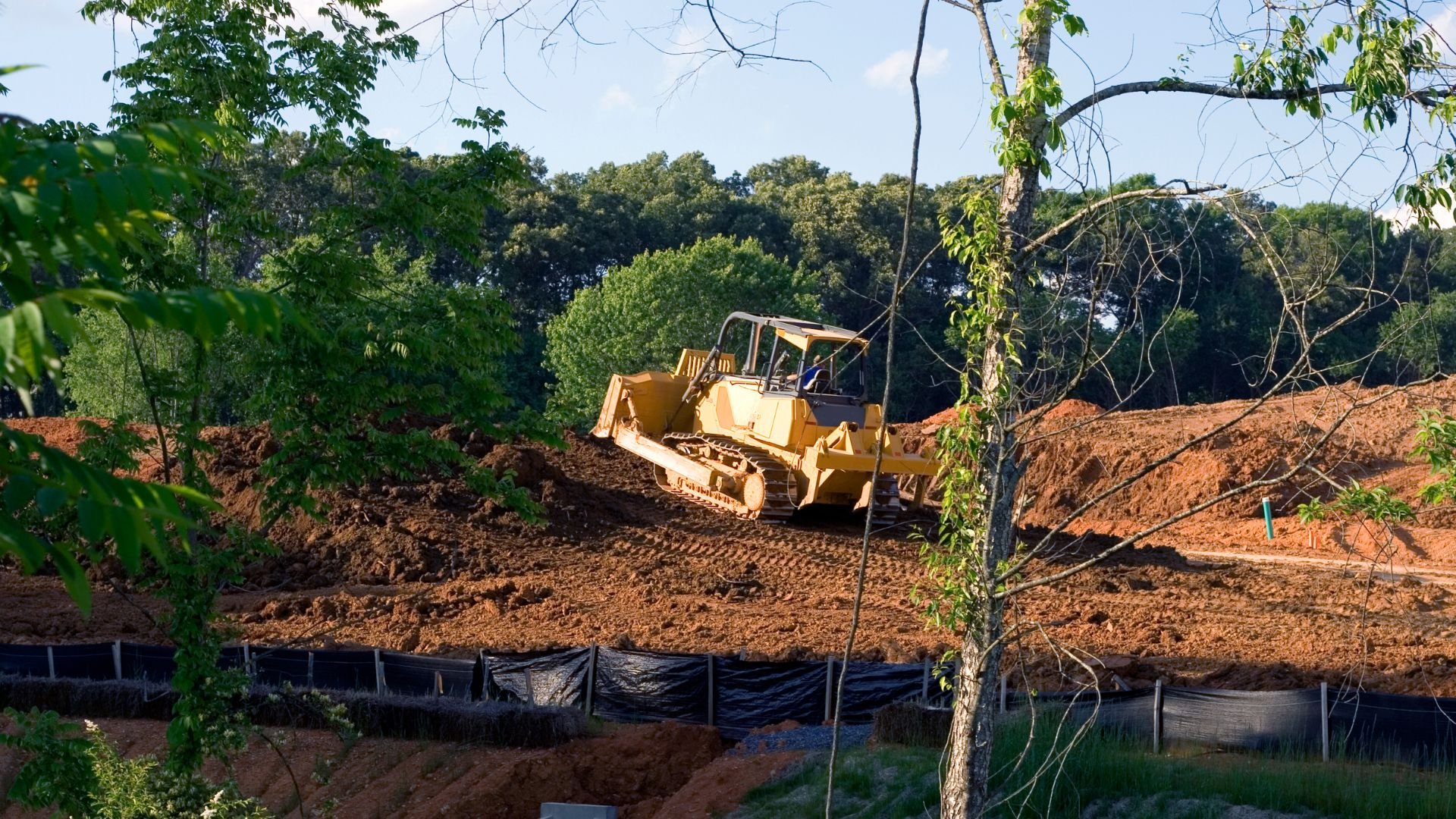 Yellow bulldozer moving earth on construction site surrounded by trees